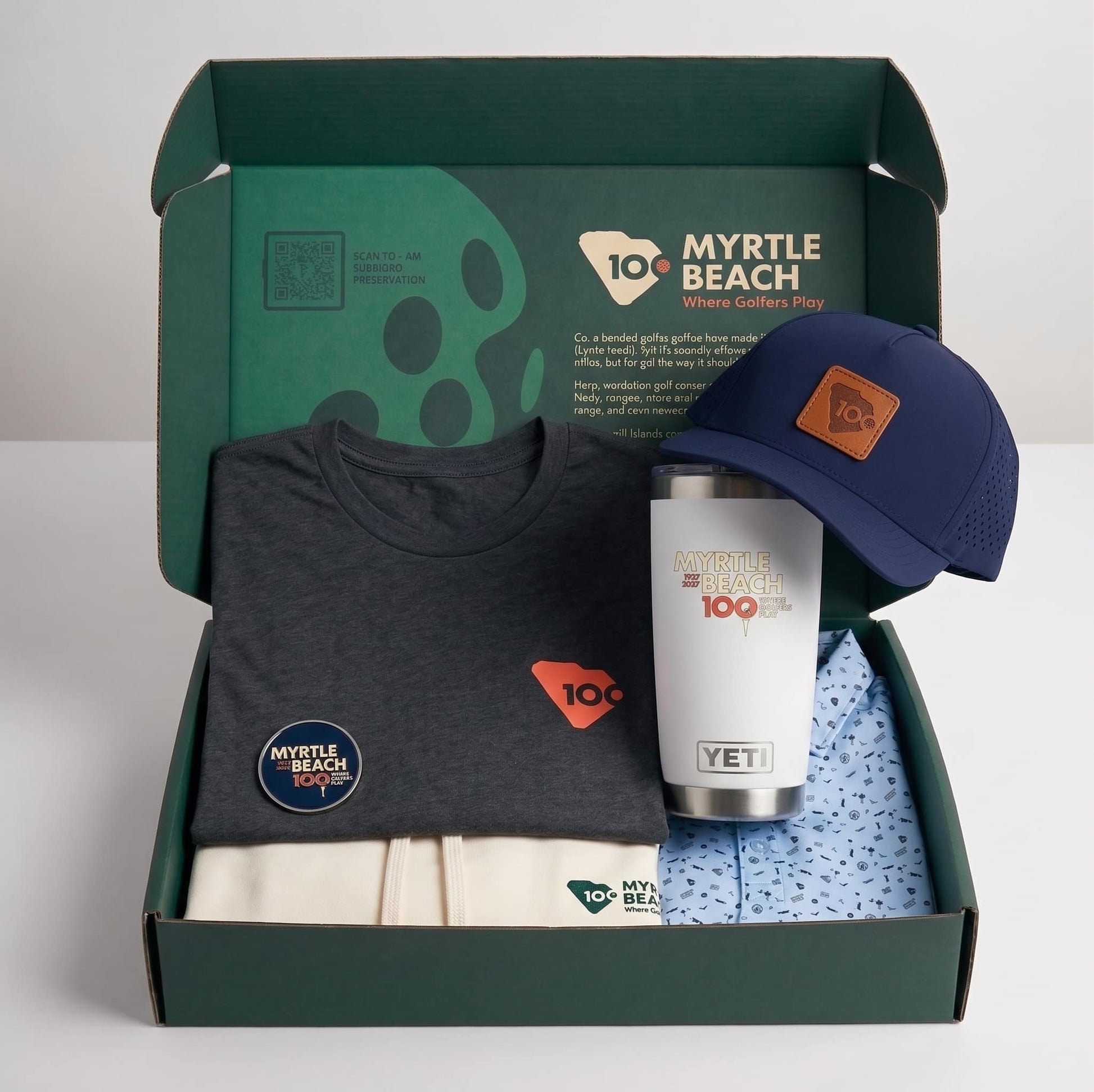 A green branded box with a grey graphic t-short, navy blue cap, white YETI mug, and blue printed polo.
