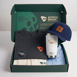 A green branded box with a grey graphic t-short, navy blue cap, white YETI mug, and blue printed polo.